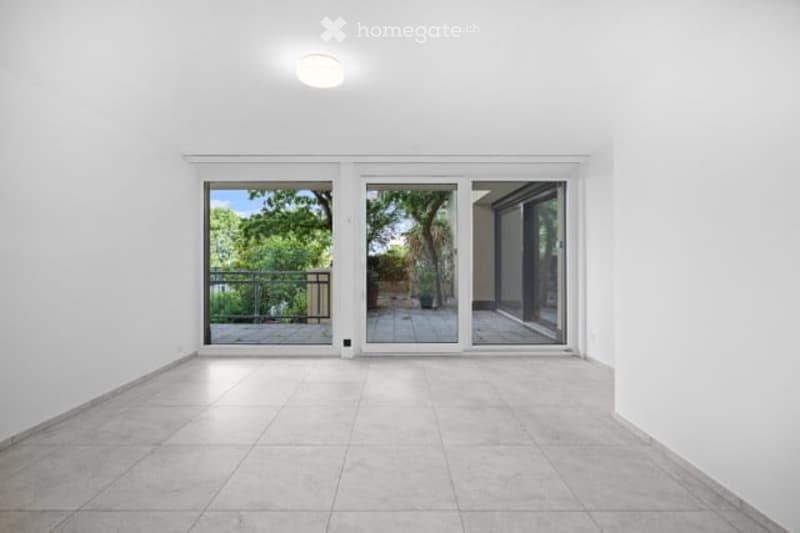 Empty room with white walls, tiled floor, large sliding glass doors leading to a balcony or terrace area with outdoor furniture visible.