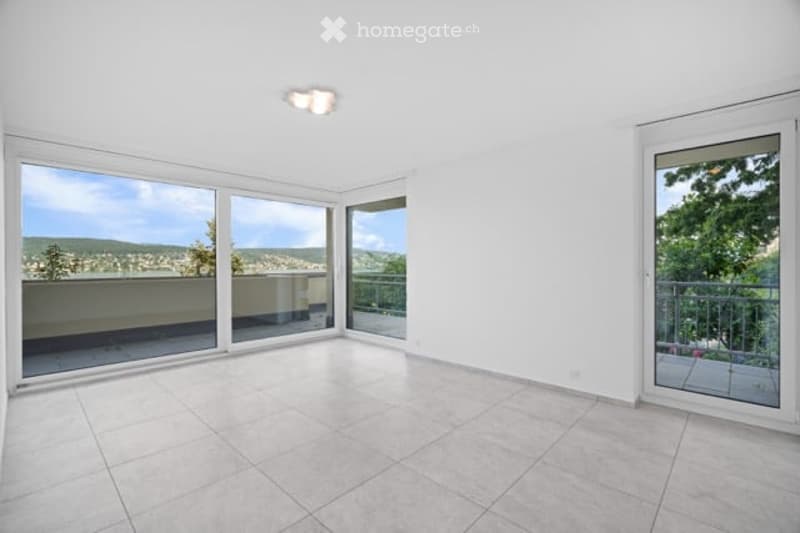 Bright, empty room with large windows and sliding glass doors leading to a balcony, offering scenic views.