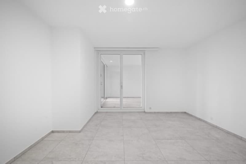 Empty room with white walls, tiled floor, and large sliding glass doors leading to another space.
