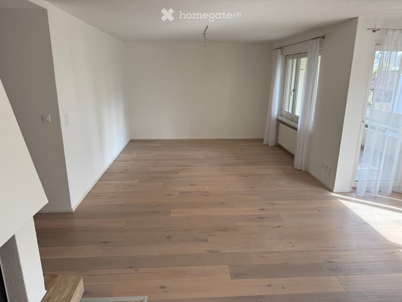 Empty room with wooden flooring, white walls, and large windows with white curtains. No furniture or equipment present.