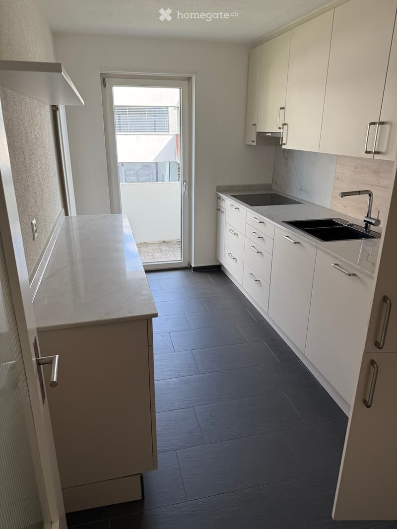 Modern kitchen with white cabinets, dark countertops, and a sink area. Features a sliding glass door leading to a balcony.