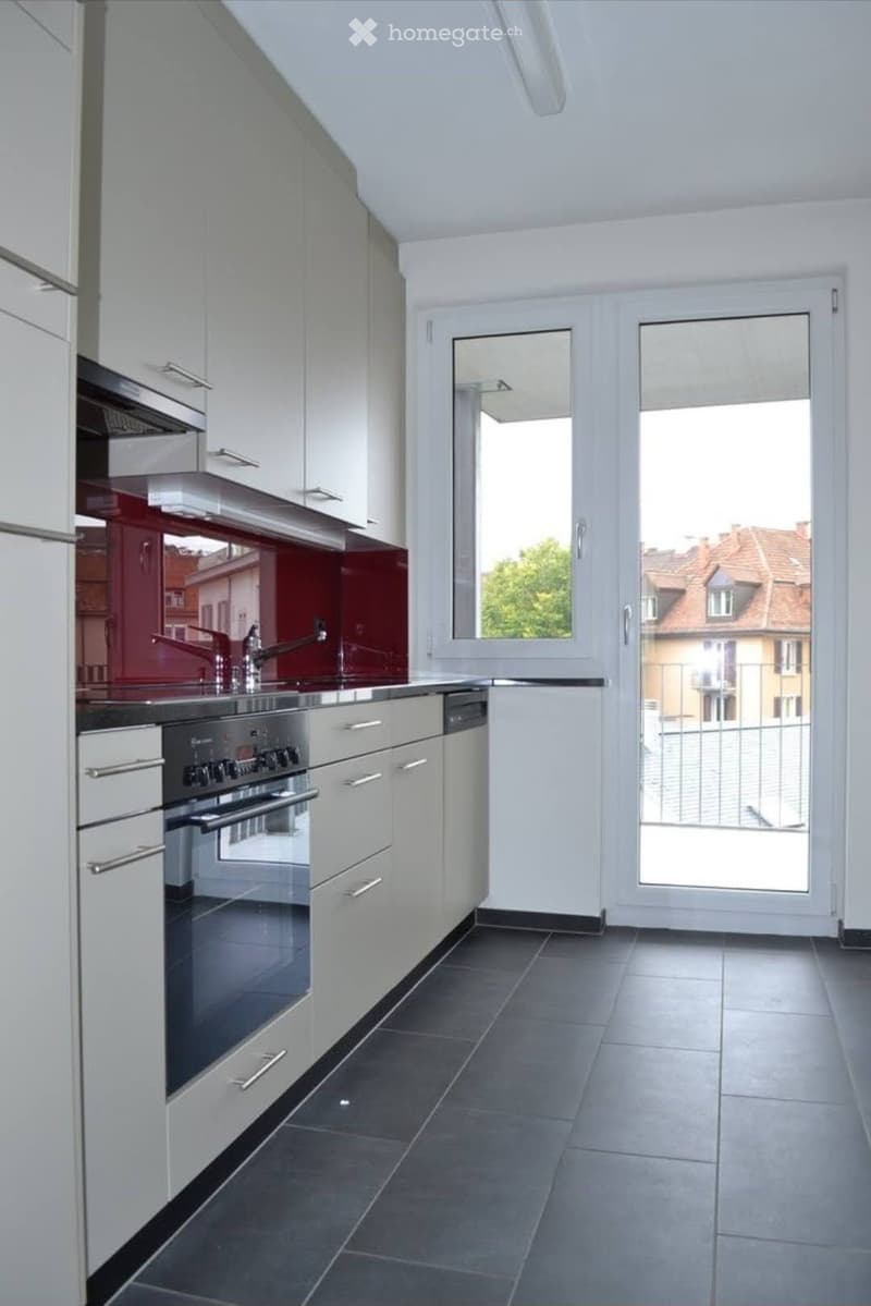 Modern kitchen with white cabinets, stainless steel appliances, and a large window overlooking a cityscape.