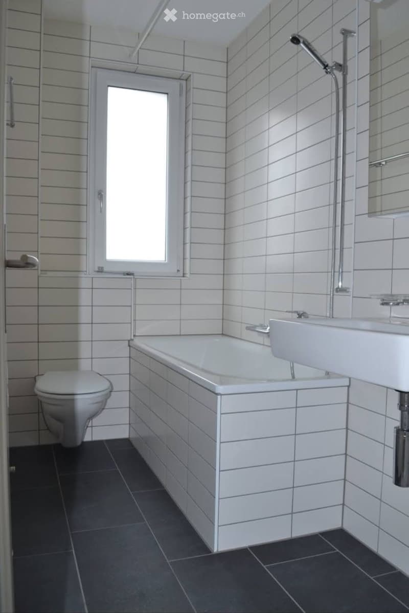 Modern bathroom with white tiled walls, dark tiled floor, bathtub, toilet, and sink.