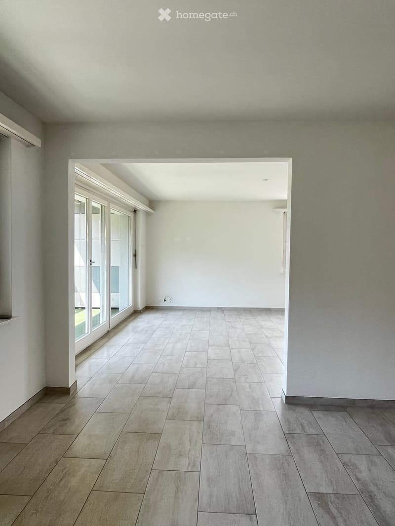 Empty room with tiled floor and white walls, featuring large glass doors leading to an outdoor area.