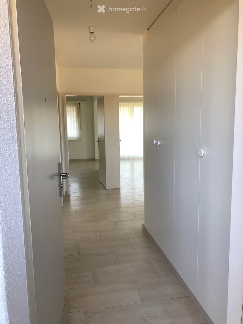 Empty hallway with tiled floor, white walls, and a single light fixture hanging from the ceiling. Doors lead to adjacent rooms.