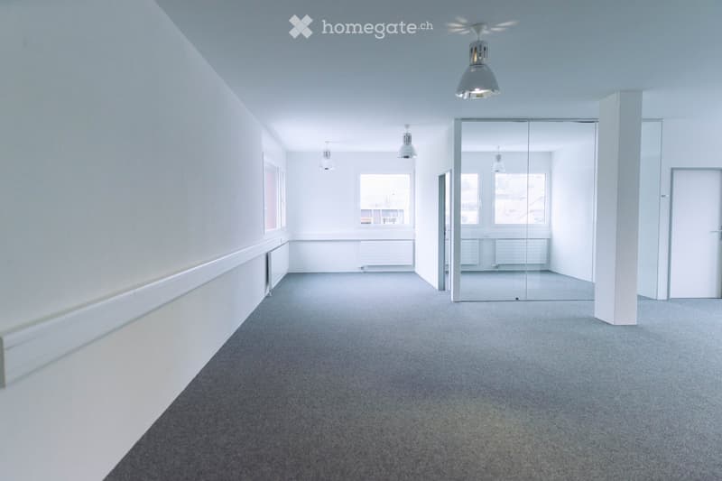 Empty room with white walls, grey carpet, large windows, and modern lighting fixtures.