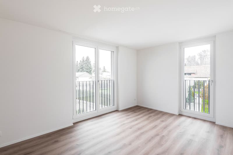 Empty room with light wooden flooring, white walls, and two large sliding glass doors leading to a balcony area.