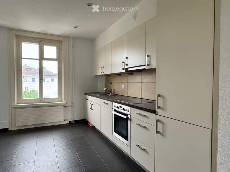 White cabinets, black countertops, stainless steel appliances, tiled floor, window with white frames, large window sill