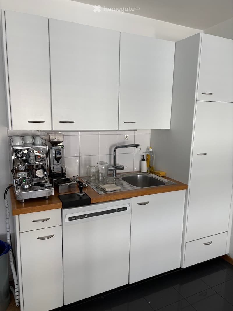 Modern kitchen with white cabinets, wooden countertops, stainless steel sink, coffee machine, and dishwasher.