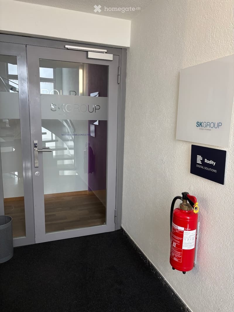 Hallway with a glass door labeled "SKGROUP" and a red fire extinguisher mounted on the wall.