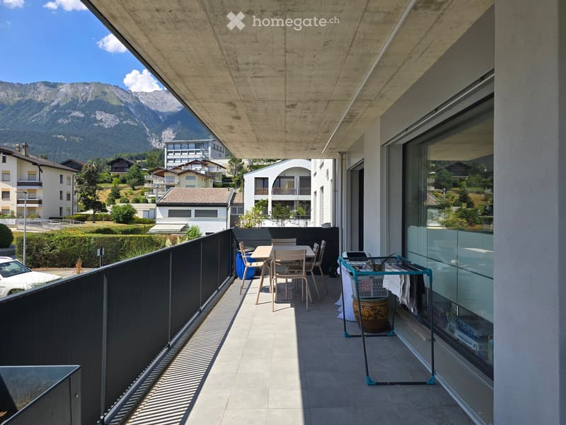 Balcony with a view of mountains, featuring a table, chairs, a stool, and a laundry rack.