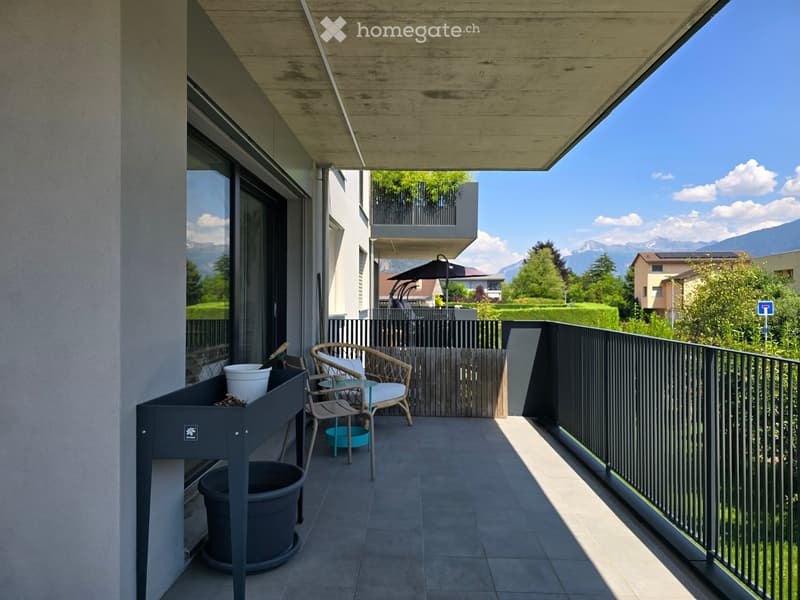 Balcony with modern furniture, including a chair, small table, and potted plants, overlooking a scenic mountain view.