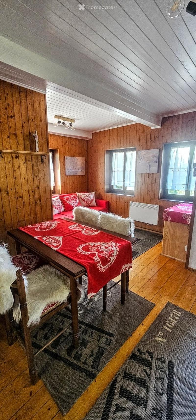 Cozy wooden-paneled room with a red sofa, dining table with chairs, and fur throw pillows.