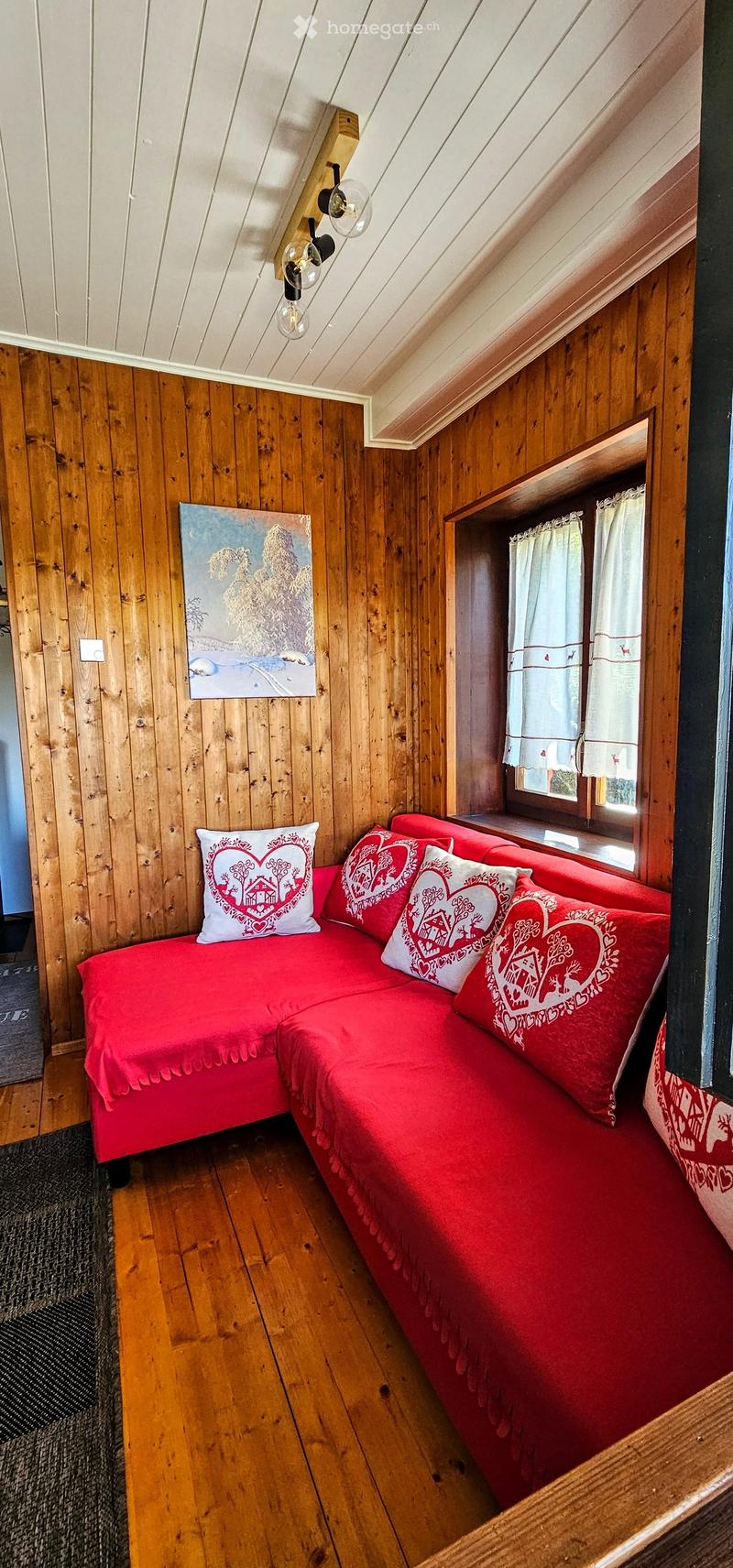 Cozy attic room with wooden walls and ceiling, red sofa with decorative pillows, and a painting on the wall.