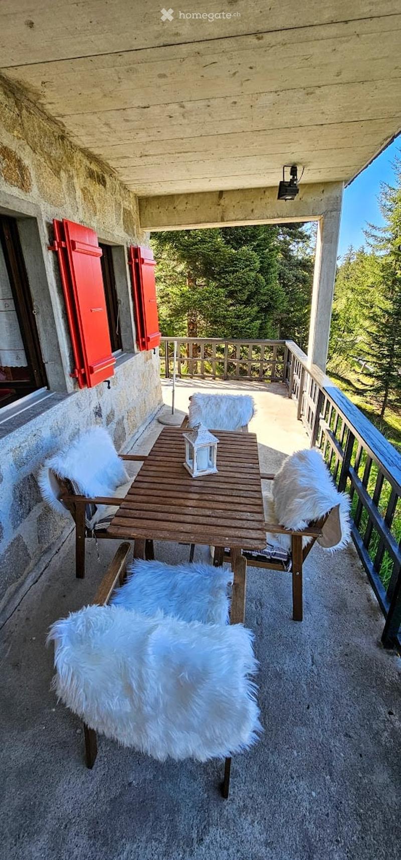 Balcony with wooden table, white fur chairs, and scenic mountain view.
