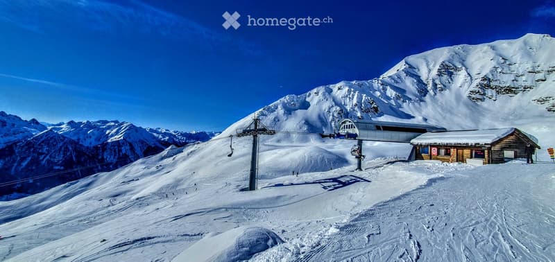 A ski lift station on a snowy mountain slope with a wooden cabin and a clear blue sky.