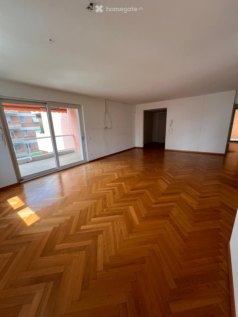 Empty room with wooden herringbone flooring, white walls, and large sliding glass doors leading to a balcony.