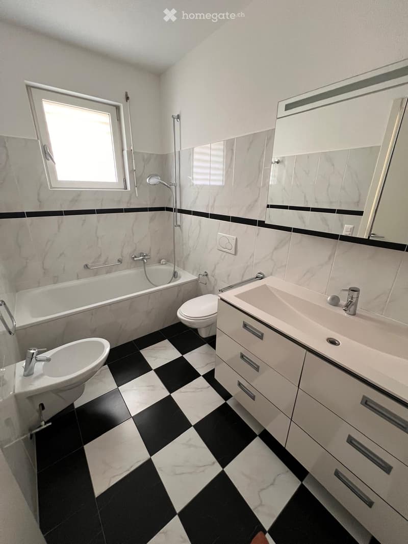 Modern bathroom with black and white checkered floor, marble tiles, bathtub, toilet, two sinks, and mirrored cabinet.