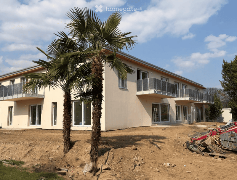 Two-story house with beige exterior, large windows, and balconies, surrounded by palm trees and construction area.