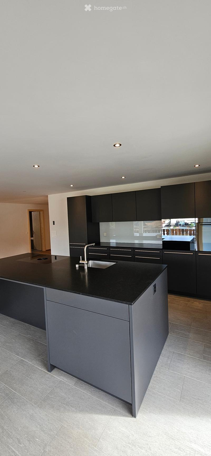 Modern kitchen with black countertops, grey cabinets, and a central island with a sink and faucet.