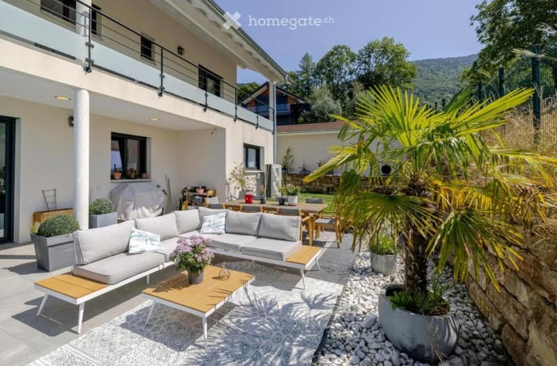 Modern house with balcony, outdoor seating area, garden with palm tree, dining table, and potted plants