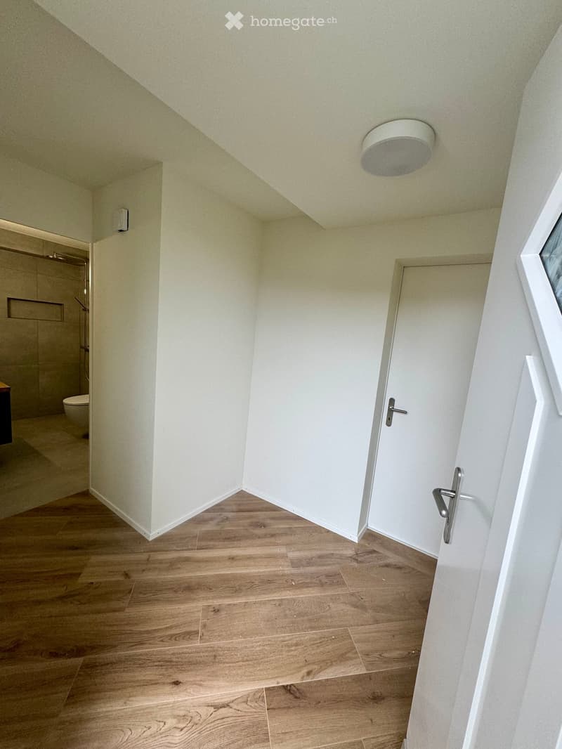 Empty hallway with wooden flooring, white walls, and a closed door leading to a bathroom area visible in the background.