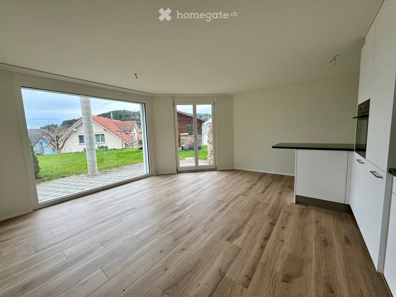 Empty room with light wooden flooring, white walls, and large glass sliding doors leading to a garden view.