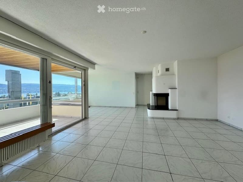 Bright, empty living space with large glass doors leading to a balcony, tiled floor, white walls, and a fireplace in the corner.