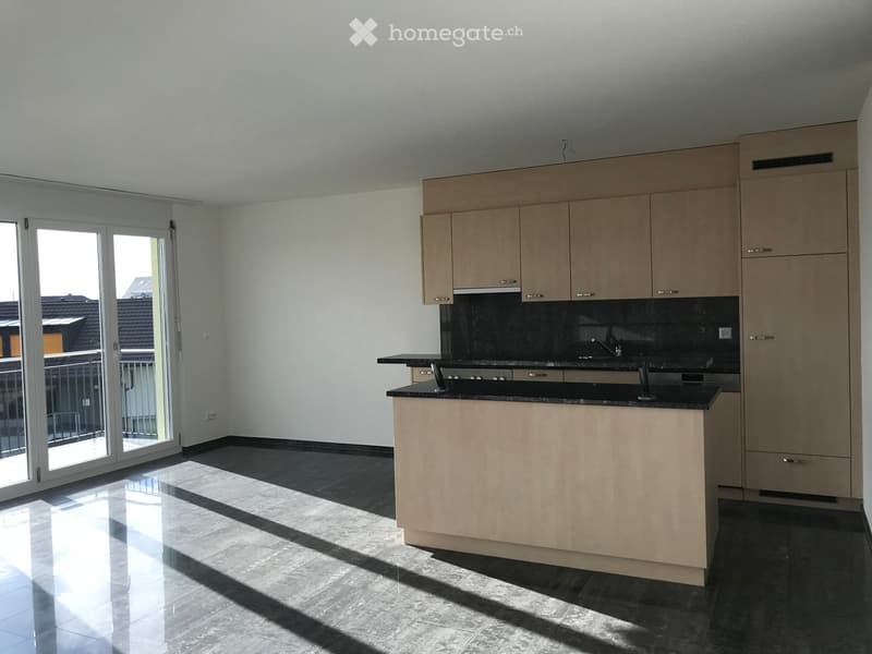 Modern kitchen with light wood cabinets, black countertop, and a large window with sliding doors leading to a balcony.