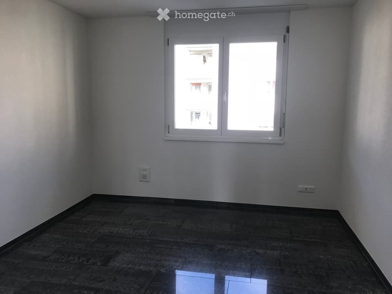 Empty room with dark tiled floor and white walls, featuring a large window with white frame and two power outlets on the walls.