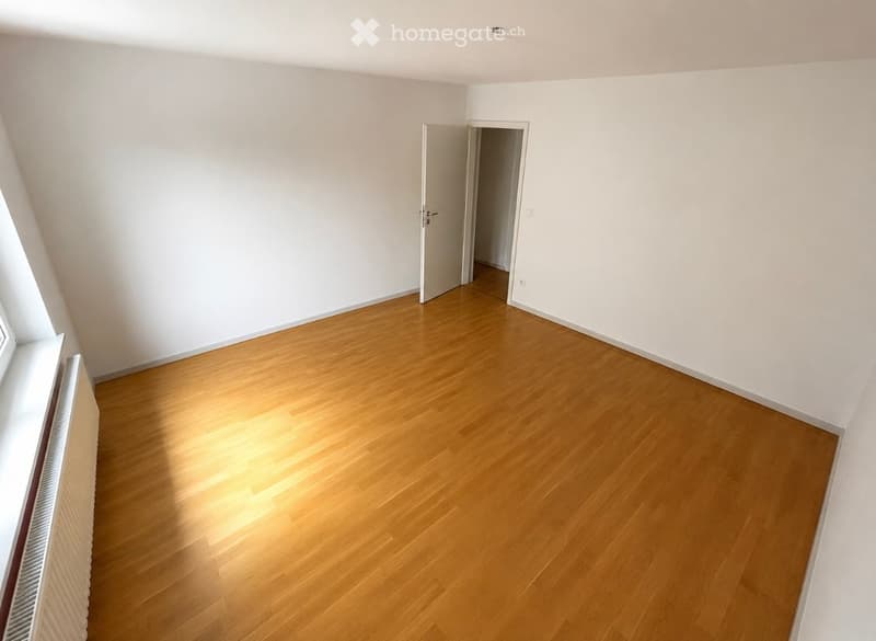 Empty room with wooden flooring and white walls, featuring a window and an open doorway leading to another space.