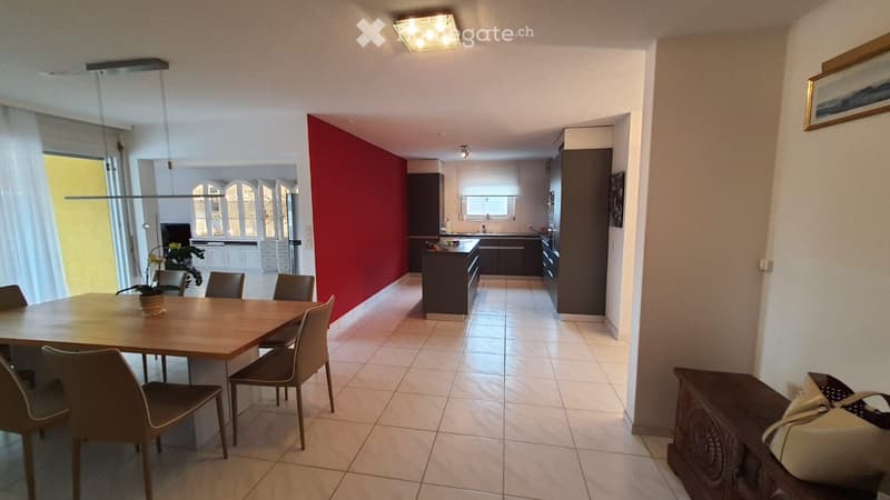 dining room with a wooden table and chairs, a wooden storage box, white walls, a red wall, and a modern kitchen with cabinets and an island countertop