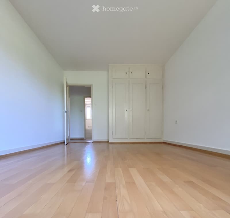 Empty room with light wooden flooring, white walls, and built-in white cabinets. An open doorway leads to another room.