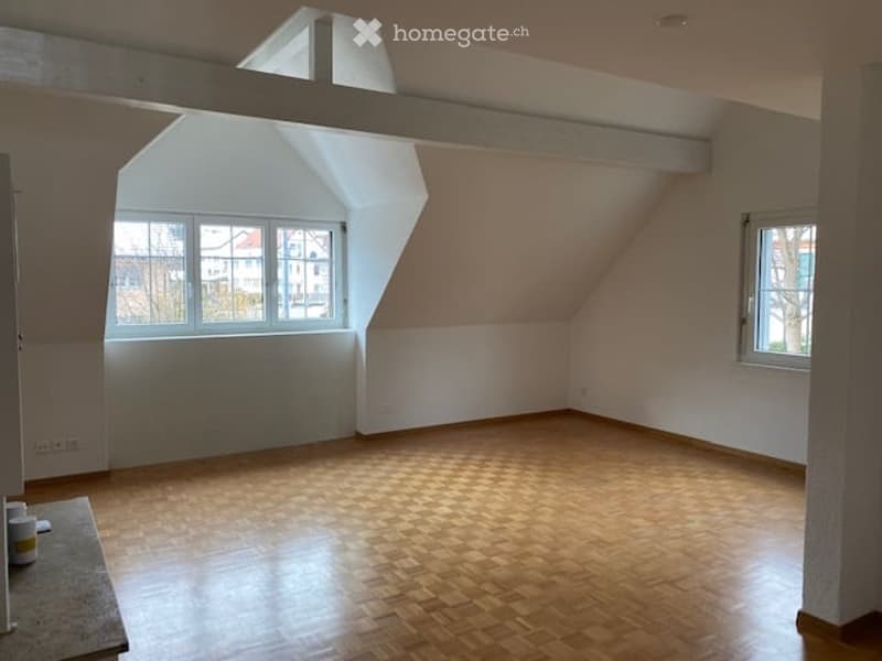 Empty attic room with wooden flooring, white walls, and large windows, featuring exposed wooden beams on the ceiling.