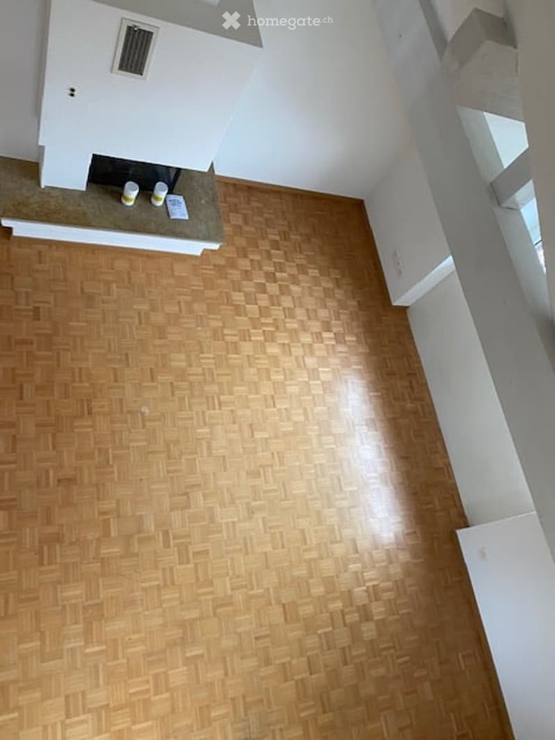 Completely empty room with wooden herringbone flooring and white walls. A fireplace is visible in the corner, but no furniture or equipment is present.