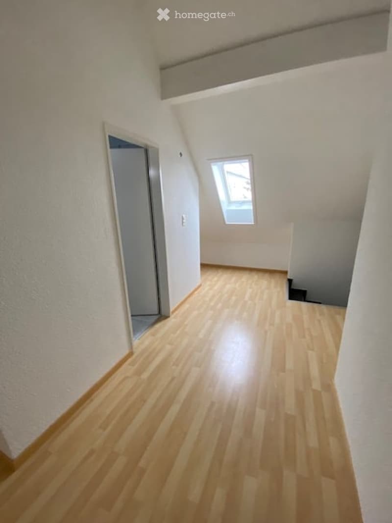Empty room with wooden flooring, white walls, and a small window at the far end.