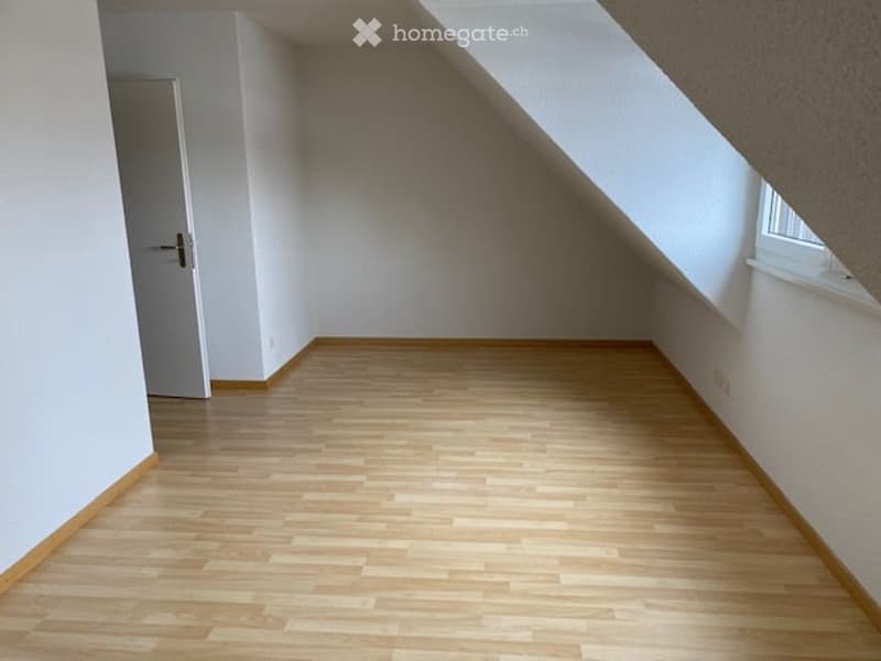 Empty room with wooden flooring, white walls, and a slanted ceiling. No furniture or equipment is present.