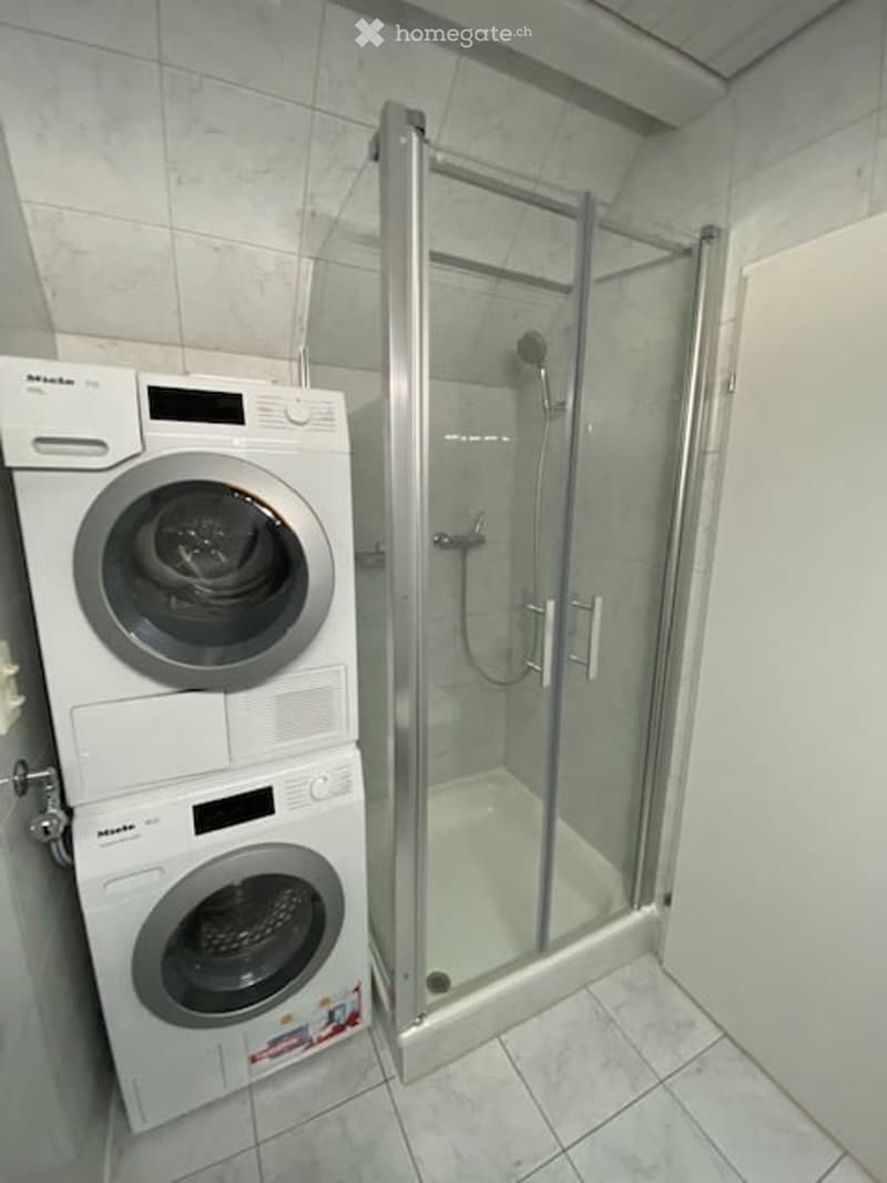 Modern bathroom with a white tiled shower stall and a stacked washing machine/dryer unit.