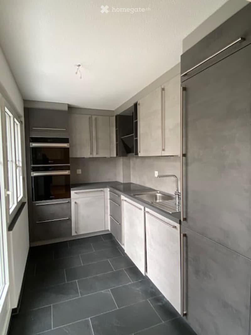 Modern kitchen with grey cabinets, stainless steel appliances, and dark tiled flooring.