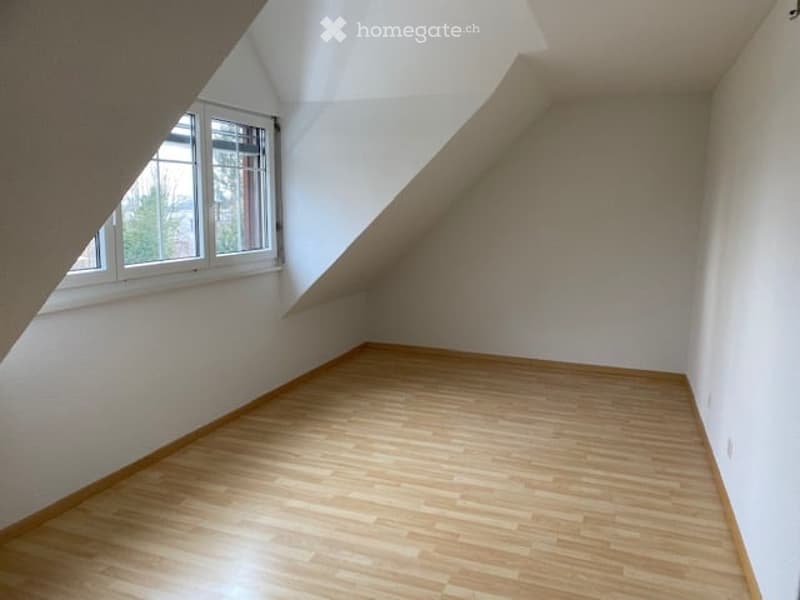 Empty attic room with wooden flooring, white walls, and a single window letting in natural light.