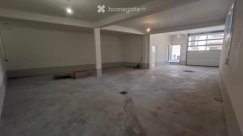 Empty room with concrete floor, white walls, and large garage door opening to an outdoor area. No furniture or equipment present.