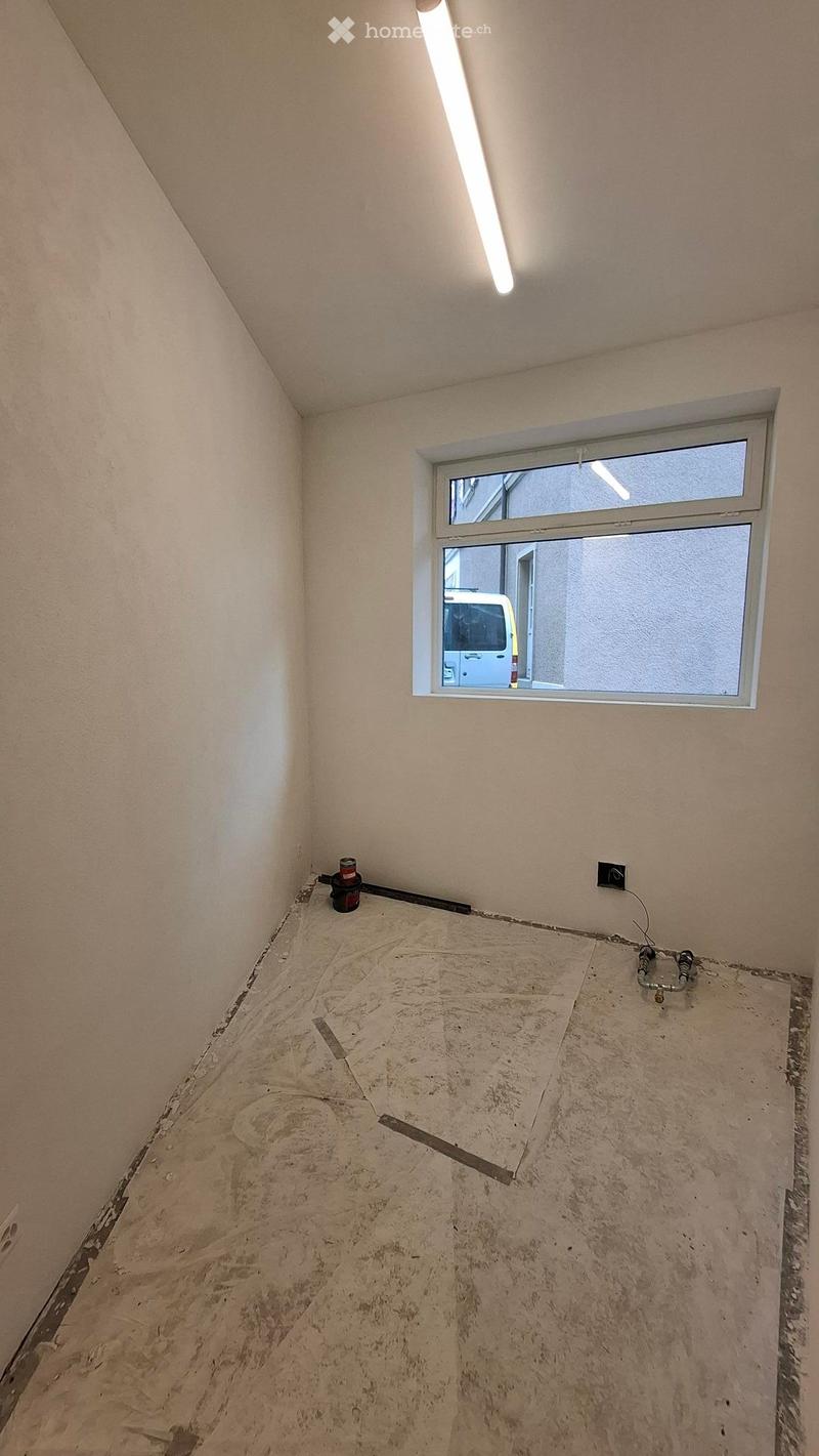 Empty room with bare walls and unfinished concrete floor, featuring a single window and exposed electrical wiring.