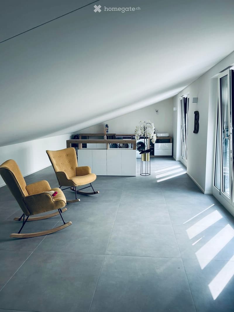 Modern, minimalist room with two rocking chairs, a small table, a cabinet, and a flower vase, featuring large windows and a sleek, grey tiled floor.