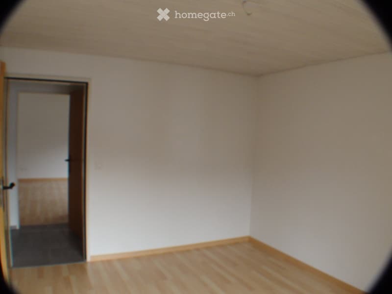 an empty room with white walls, wooden floor, an open door leading to another room