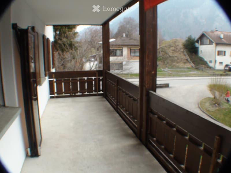 Balcony with wooden railings, concrete floor, views of the mountains and the road.
