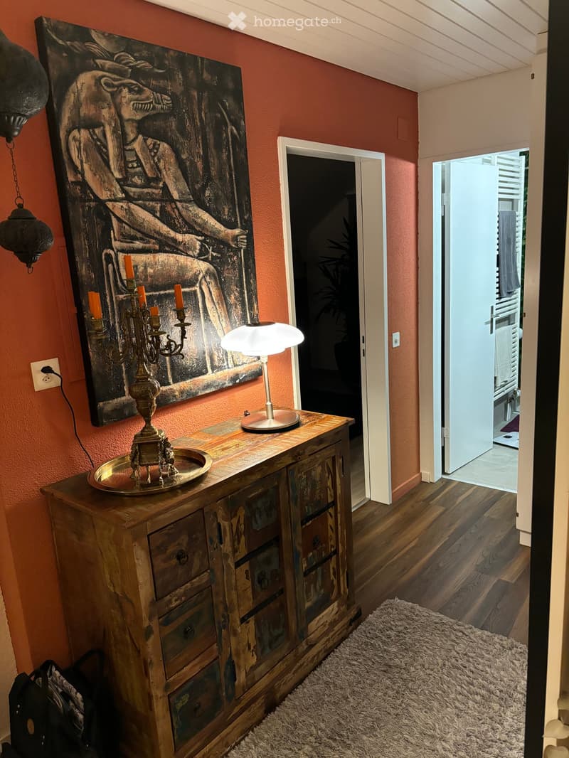 A hallway with a wooden cabinet, a table lamp, a candle holder, a painting, and a rug on the floor.