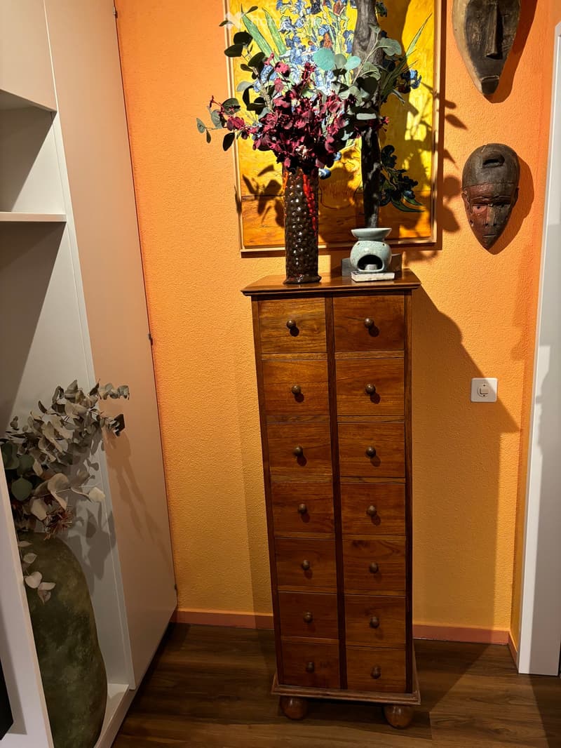 A hallway with a wooden cabinet, vase with flowers, painting, and decorative sculpture on the wall.