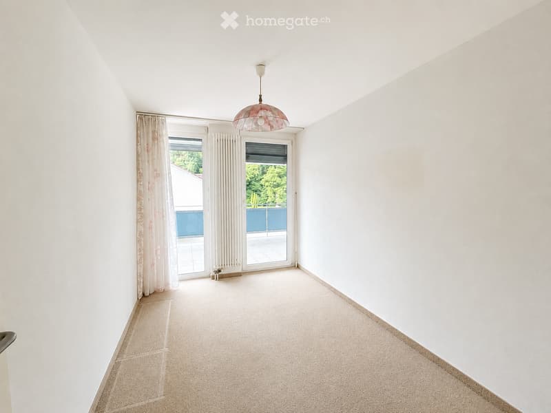 Empty room with white walls, beige carpet, large windows, and a hanging light fixture. The room has a sliding glass door leading to a balcony.