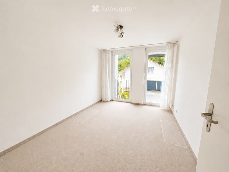 Empty room with white walls, carpeted floor, and large sliding glass doors leading to a balcony or outdoor area.