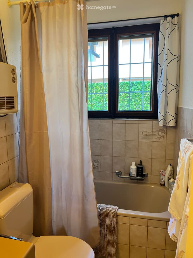 Bathroom with bathtub, toilet, shower curtain, towel, and toiletries on the shelf